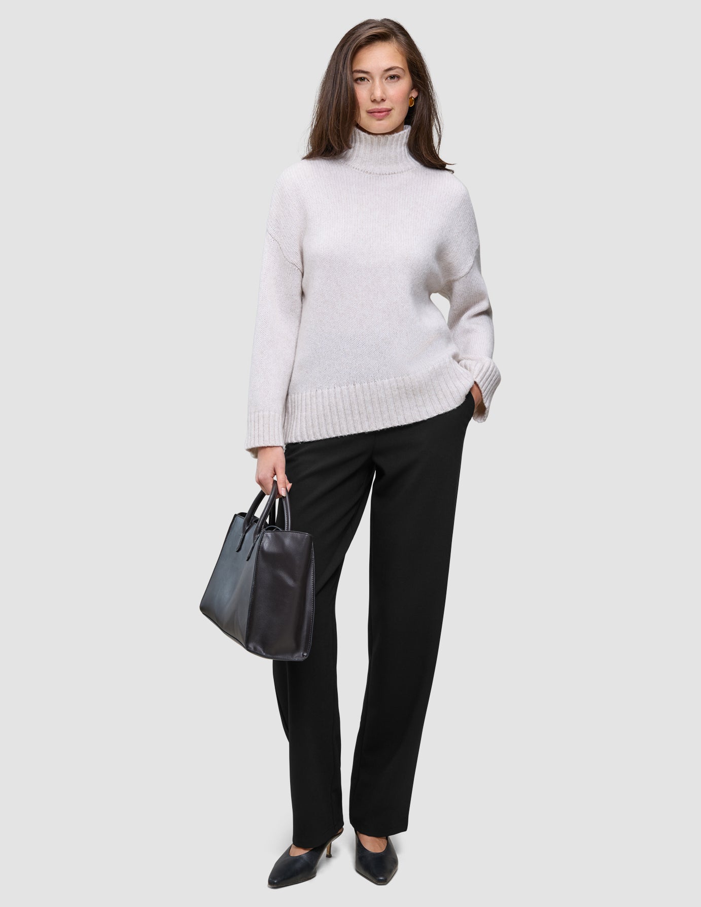 En kvinne i en lys turtleneck og Women GO2 Pants Straight Black, som holder en håndveske i minimalistisk skandinavisk stil.